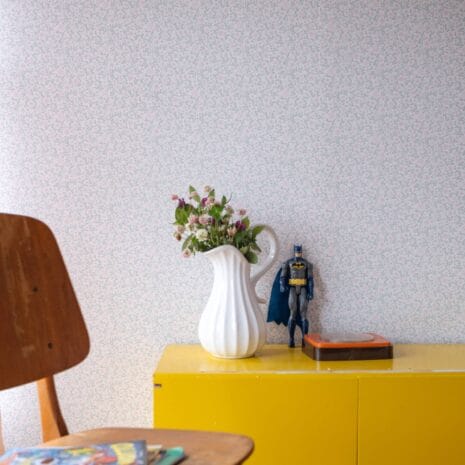 Oili 3 Tapetissa on pieniä vaaleanpunaisia kukkia ja vihreitä lehtiä valkoisella pohjalla.