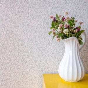 Tapetissa on pieniä vaaleanpunaisia kukkia ja vihreitä lehtiä valkoisella pohjalla.